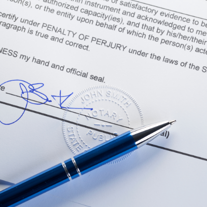 Close-up of a signed document with a blue pen resting on it and an embossed notary seal visible near the signature line.