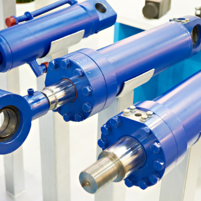 Close-up of several blue hydraulic cylinders with shiny metal piston rods and bolted end caps, displayed on a stand as industrial machinery components.