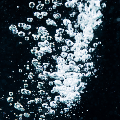 Close-up view of numerous water bubbles forming a bright, swirling column against a deep blue background.
