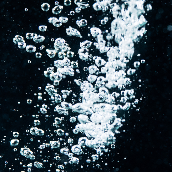 Close-up view of numerous water bubbles forming a bright, swirling column against a deep blue background.