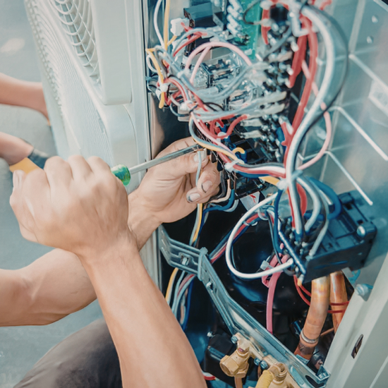 A technician uses a screwdriver to work on the internal wiring and components of an HVAC unit, with colorful electrical wires, circuit boards, and copper pipes visible inside the open panel.