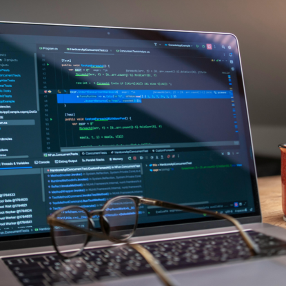 Close-up of a laptop displaying a code editor with programming code, with a pair of eyeglasses resting on the keyboard in the foreground.