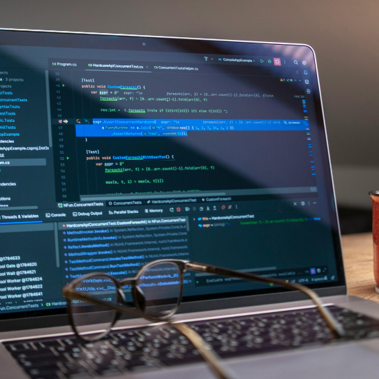 Close-up of a laptop displaying a code editor with programming code, with a pair of eyeglasses resting on the keyboard in the foreground.